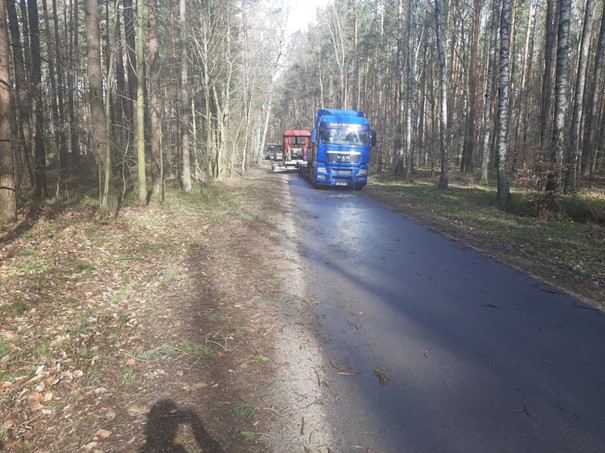 Na zdjęciu droga w lesie a na niej samochód ciężarowy oraz maszyny budowlane.